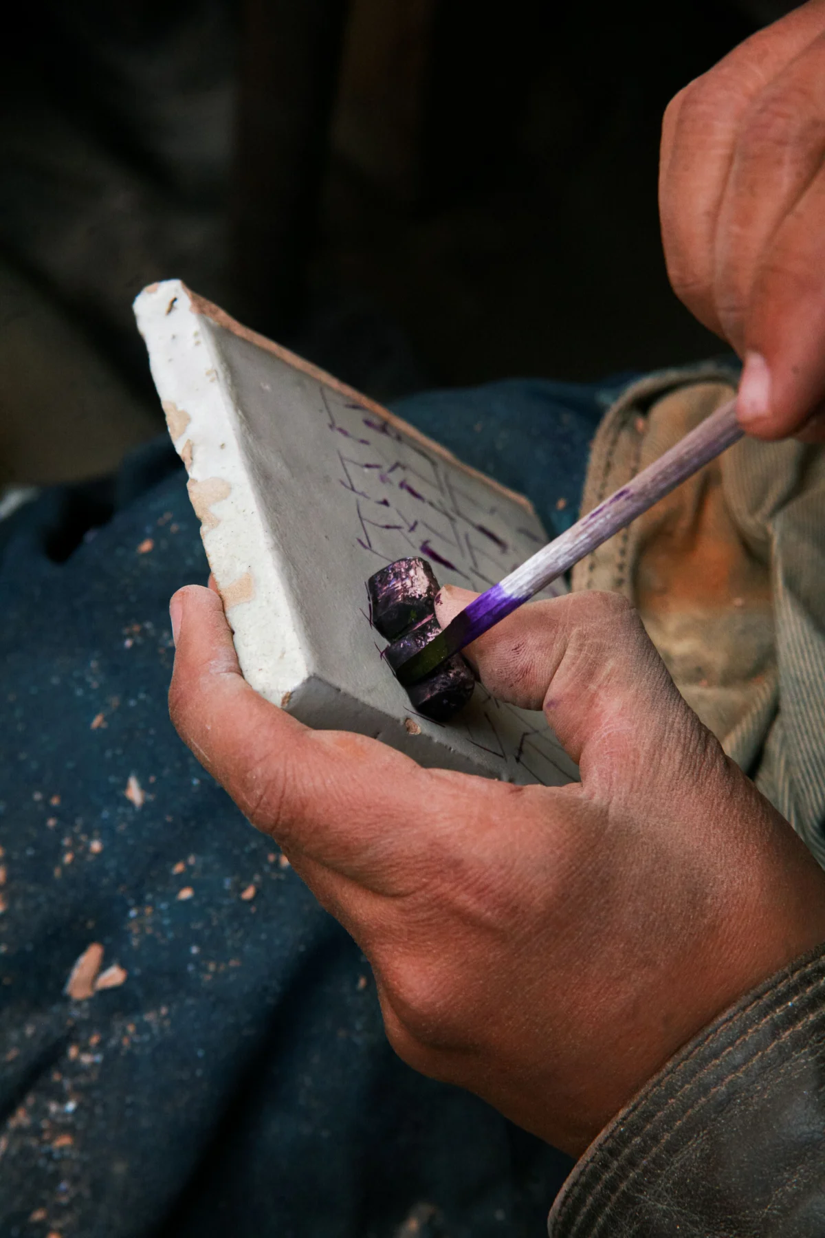 Main d’un artisan peignant un motif sur un carreau de céramique à Fès